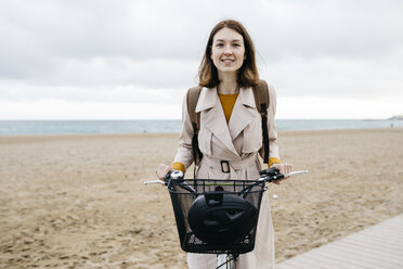 Porträt einer lächelnden Frau mit E-Bike am Strand - JRFF02979