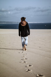Young man walking away in the dunes, rear view - OCMF00362
