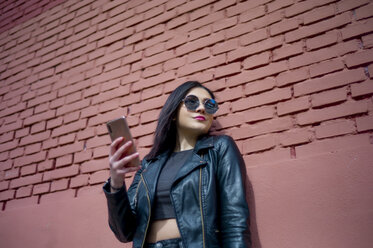 Portrait of young woman with smartphone wearing sunglasses and black leather jacket - OCMF00370