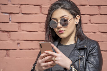 Porträt einer jungen Frau mit Sonnenbrille und schwarzer Lederjacke, die auf ihr Smartphone schaut - OCMF00375