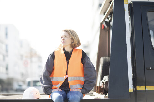 Frau mit reflektierender Weste sitzt auf der Ladefläche eines Lastwagens - SGF02355