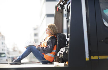 Frau mit reflektierender Weste sitzt auf der Ladefläche eines Lastwagens - SGF02356