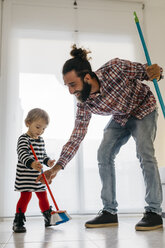 Happy father and little daughter sweeping the floor of the living room at home - JRFF02985