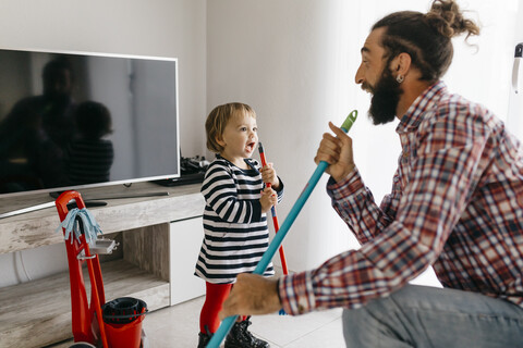 Vater und kleine Tochter haben Spaß zusammen beim Aufräumen des Wohnzimmers, lizenzfreies Stockfoto