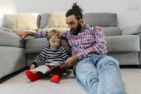Vater und kleine Tochter sitzen auf dem Fußboden im Wohnzimmer und lesen gemeinsam ein Buch - JRFF02988