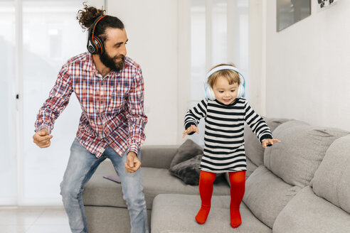 Vater und kleine Tochter tanzen im Wohnzimmer, während sie mit Kopfhörern Musik hören - JRFF02990