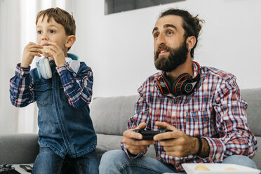 Portrait of father and son on the couch playing computer game - JRFF02994