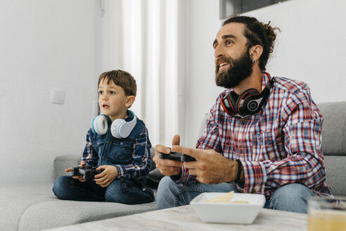 Porträt von Vater und Sohn, die zusammen auf der Couch sitzen und ein Computerspiel spielen - JRFF02995