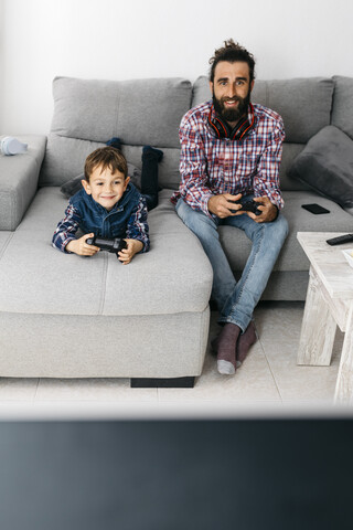 Porträt von Vater und Sohn, die zusammen auf der Couch ein Computerspiel spielen, lizenzfreies Stockfoto