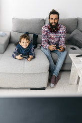 Porträt von Vater und Sohn, die zusammen auf der Couch ein Computerspiel spielen - JRFF03002