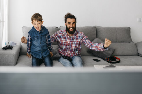 Porträt von Vater und Sohn, die zusammen auf der Couch ein Computerspiel spielen - JRFF03003