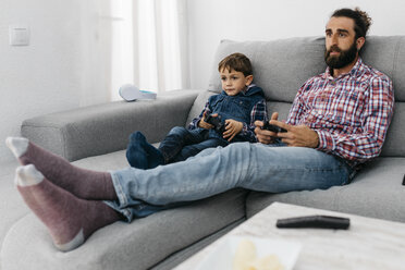 Porträt von Vater und Sohn, die zusammen auf der Couch sitzen und ein Computerspiel spielen - JRFF03004