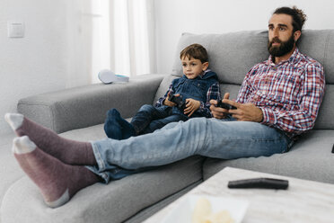 Portrait of father and son sitting together on the couch playing computer game - JRFF03004