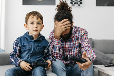 Vater und Sohn sitzen zusammen auf der Couch und spielen ein Computerspiel - JRFF03006