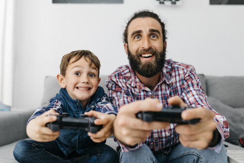 Porträt von Vater und Sohn, die zusammen auf der Couch sitzen und ein Computerspiel spielen - JRFF03007