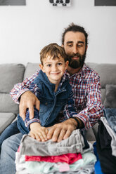 Porträt von Vater und Sohn, die zusammen auf der Couch sitzen und Wäsche zusammenlegen - JRFF03010