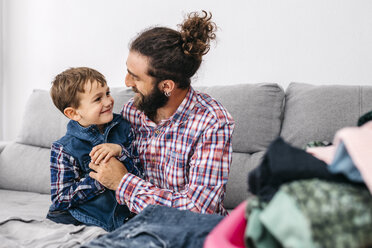 Vater und Sohn sitzen zusammen auf der Couch und falten Wäsche - JRFF03012