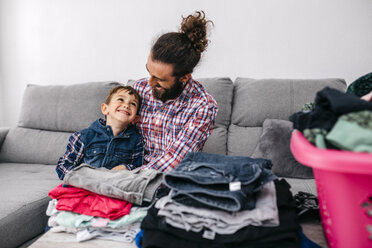 Vater und Sohn sitzen zusammen auf der Couch und haben Spaß beim Zusammenlegen der Wäsche - JRFF03013