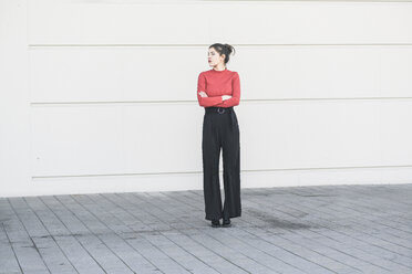 Elegant young woman standing at a wall with crossed arms - UUF17035