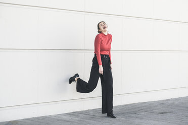 Laughing young woman leaning against a wall - UUF17048