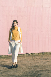 Happy young woman twinkling in front of a pink wall - UUF17066