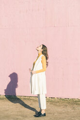 Glückliche junge Frau genießt den Sonnenschein vor einer rosa Wand - UUF17067