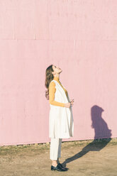 Junge Frau blickt vor einer rosa Wand nach oben - UUF17068