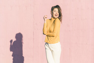 Happy young woman in front of a pink wall - UUF17076