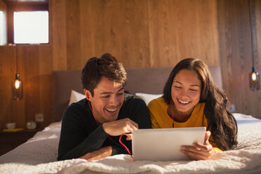Glückliches junges Paar mit Kopfhörern und digitalem Tablet auf dem Bett - HOXF04334