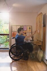 Männlicher Künstler im Rollstuhl malt im Kunstatelier - HOXF04378