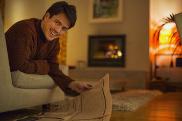 Porträt eines lächelnden Mannes, der im Wohnzimmer Zeitung liest - HOXF04385