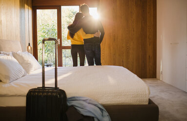 Paar mit Koffer, das sich im Schlafzimmer umarmt - HOXF04401
