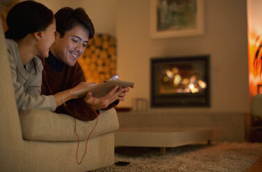 Happy couple with headphones sharing digital tablet on living room sofa - HOXF04408