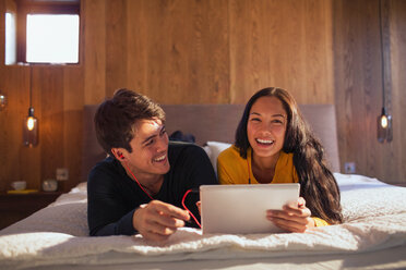 Porträt eines glücklichen Paares mit Kopfhörern und gemeinsamem Laptop auf dem Bett - HOXF04415