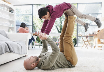 Mann hebt Frau auf Beinen liegend auf Sofa im Wohnzimmer zu Hause,  lizenzfreies Stockfoto