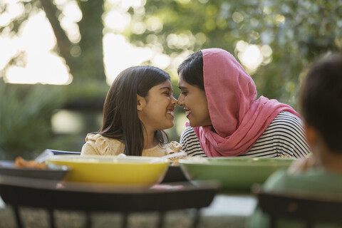 Liebevolle Mutter im Hidschab reibt Nasen am Esstisch, lizenzfreies Stockfoto