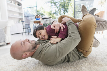 Playful father and son hugging on floor - CAIF23146