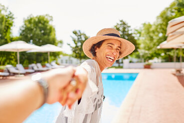 Glückliche Frau führt ihren Mann an der Hand am sonnigen Pool des Resorts - CAIF23148