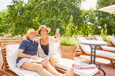 Glückliches reifes Paar, das ein Selfie mit einem Fotohandy in einem sonnigen Resort am Pool macht - CAIF23159