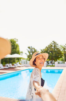 Glückliche Frau führt ihren Mann an der Hand am sonnigen Pool des Resorts - CAIF23162