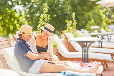 Ein Paar entspannt sich, liest ein Buch und benutzt sein Smartphone auf einem Liegestuhl am Pool des Resorts - CAIF23171