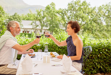Älteres Paar stößt mit Weingläsern am Tisch eines Terrassenrestaurants an - CAIF23175