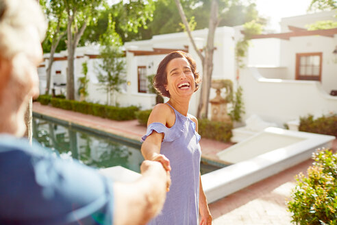 Glückliches, sorgloses reifes Paar, das sich am Pool eines sonnigen Resorts an den Händen hält - CAIF23187