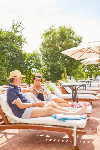 Älteres Paar entspannt sich, liest auf Liegestühlen am sonnigen Pool des Resorts, lizenzfreies Stockfoto