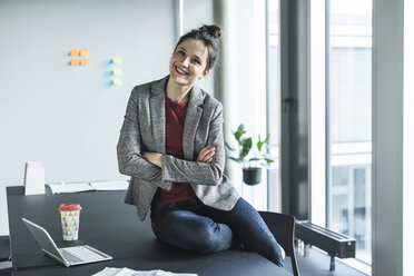 Portrait of smiling businesswoman sitting on desk in office - UUF17081