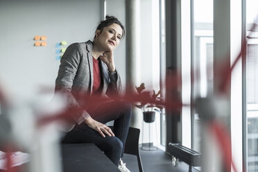 Porträt einer Geschäftsfrau, die auf einem Schreibtisch im Büro sitzt - UUF17086