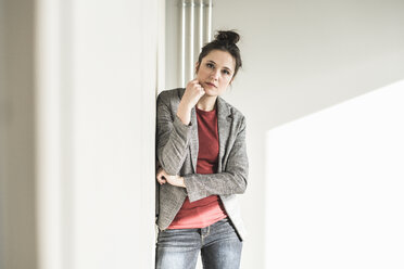 Portrait of serious businesswoman leaning against a wall in office - UUF17097