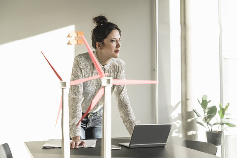 Businesswoman with wind turbine models and laptop on desk in office stock photo
