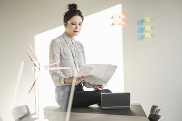 Geschäftsfrau im Büro beim Lesen eines Plans mit Windkraftanlagenmodellen auf dem Schreibtisch - UUF17113