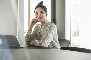 Porträt einer lächelnden Geschäftsfrau mit Laptop, die an einem Schreibtisch im Büro sitzt - UUF17114